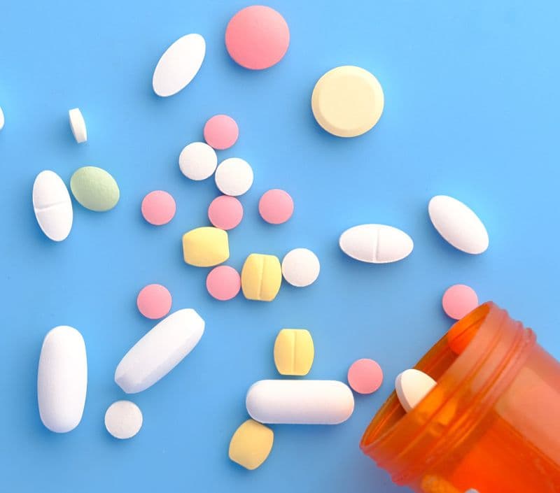 Pill bottle open with spilled pills on a light blue surface